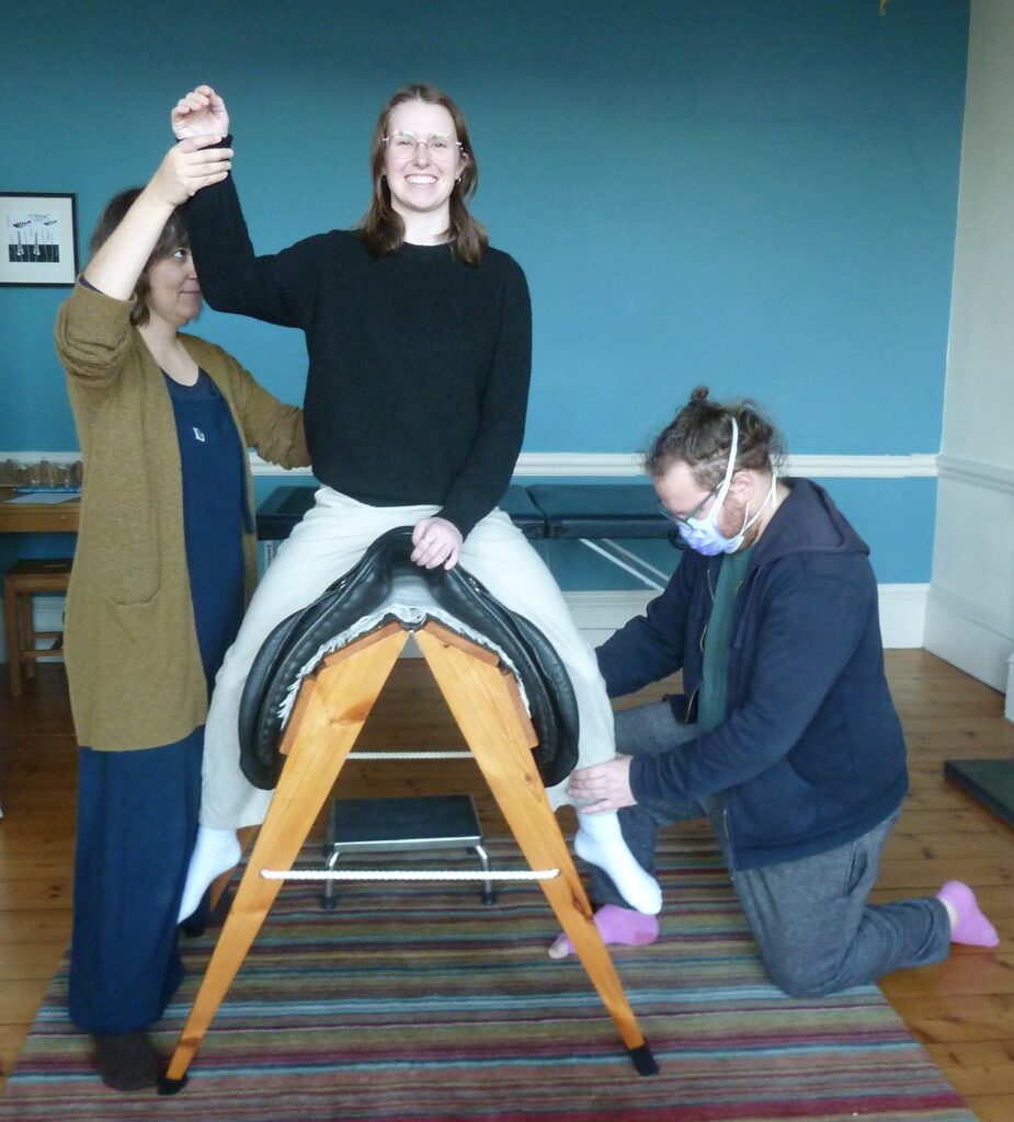 Photo of teachers working with a trainee sitting on a wooden horse